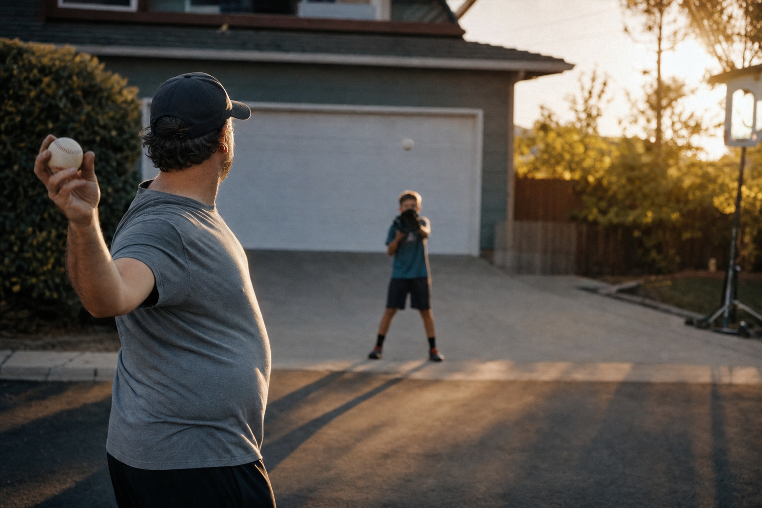 A dad playing catch with his son in the driveway at golden hour.
